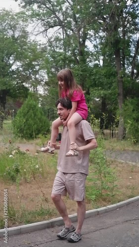 Young father carrying his happy daughter on his shoulders while walking in an amusement park