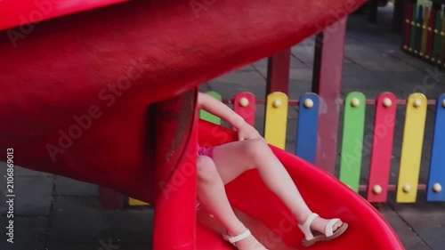 Cheerful little girl enjoying a fun summer day by sliding down a red slide at the playground