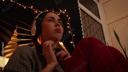Low angle view of a young Caucasian woman wearing headphones, listening to music and staring blankly into the distance while repeatedly touching her braided hair. Anxiety, neurotic behavior