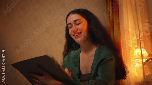 Low angle portrait of a beautiful young Caucasian woman with braces smiling softly while watching an online stream at home in the evening. Digital entertainment, relaxation