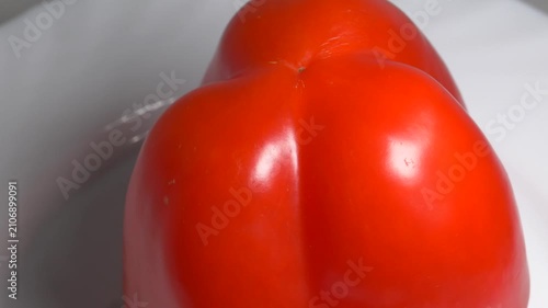 Close-up of a fresh red bell pepper rotating on a white plate, showcasing its smooth, shiny skin and vibrant color under bright studio lighting.