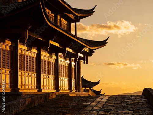 Traditional East Asian temple structure at sunset with golden light illuminating wooden architecture and tiled roof