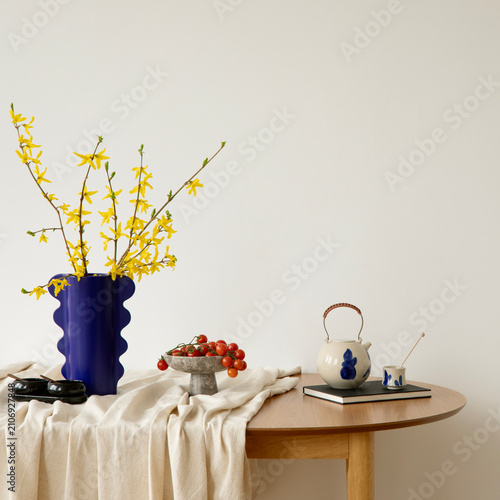 Minimalist dining area with wooden table, linen cloth and bold blue vase of yellow flowers. Bright and elegant modern composition.