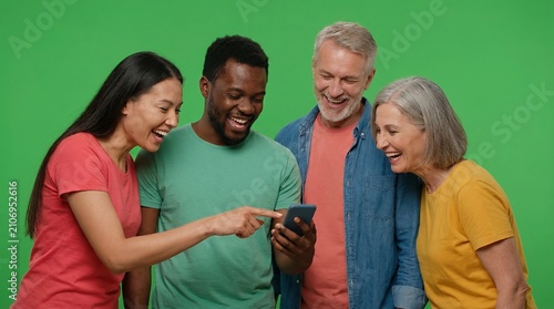 Diverse group of happy multi-generational friends laughing while looking at a smartphone screen against a green background
