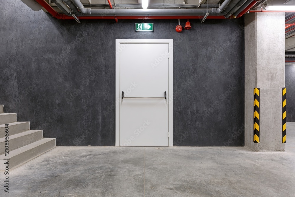 Obraz premium The White Industrial Door in a Concrete Basement Corridor with Staircase