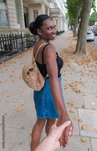 Smiling Young Black British Woman Holding Her Partner's Hand and Leading Him Along a London Street
