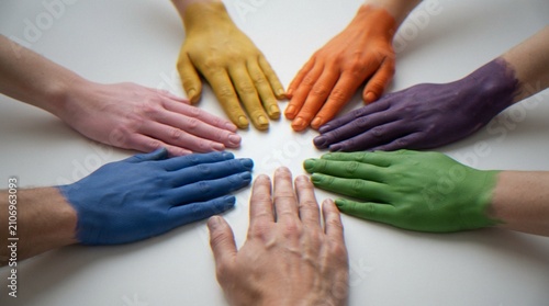 Konstfotografi A top-down view of several hands painted in different colors, arranged in a circular formation pointing toward the center on a white background, representing unity, diversity, and teamwork