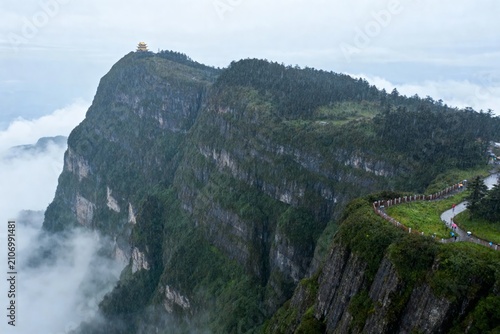 Majestic mountain peak with winding path and temple atop, surrounded by clouds and dense forest