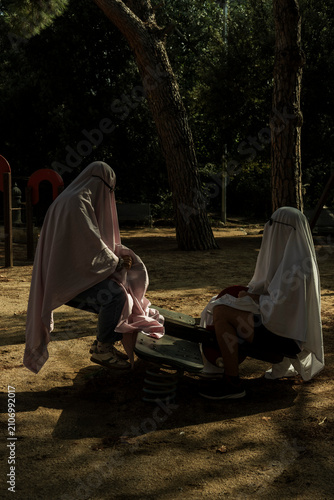Two People Dressed as Ghosts on a Playground Seesaw