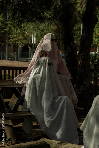 Two People Dressed as Ghosts with Sunglasses Sitting on a Park Bench
