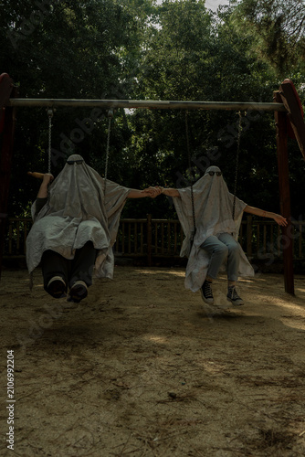 People Dressed as Ghosts Swinging on Playground Swings