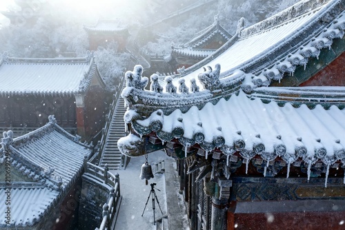 Snow-covered traditional Chinese temple rooftops with intricate eaves and icicles hanging during a winter snowfall