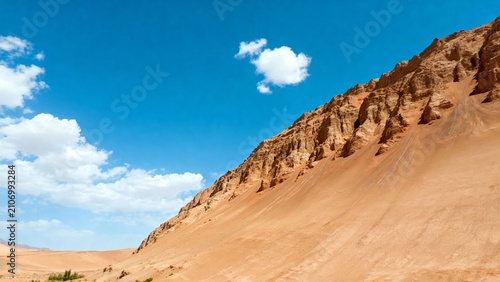 Desert landscape with sandy dunes and rocky cliffs under a clear blue sky