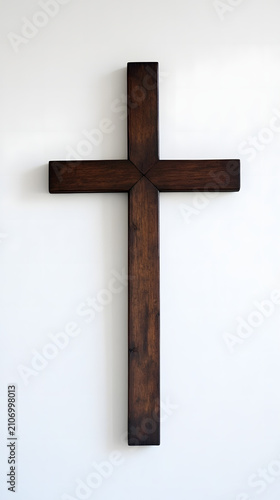 Cross made of dark polished wood stands centered against a clean and bright white wall background.
