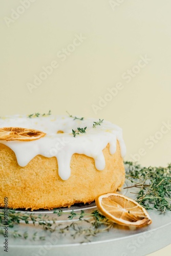 Fotografie Freshly baked lemon bundt cake decorated with white sugar glaze, dried lemon slices, and fresh thyme sprigs served on a cake stand