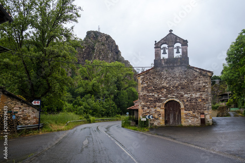An ancient stone church with a traditional bell gable situated on a winding mountain road section along the Camino Primitivo route in Asturias, Spain