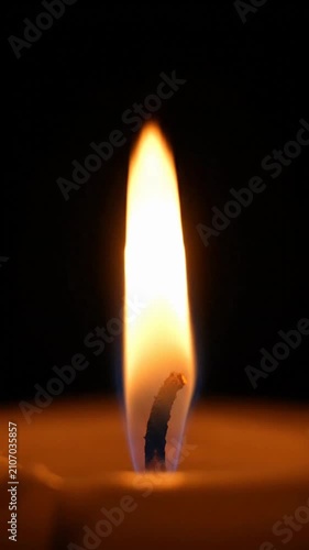 Close-up of a single candle flame burning brightly with a warm orange glow against a dark background