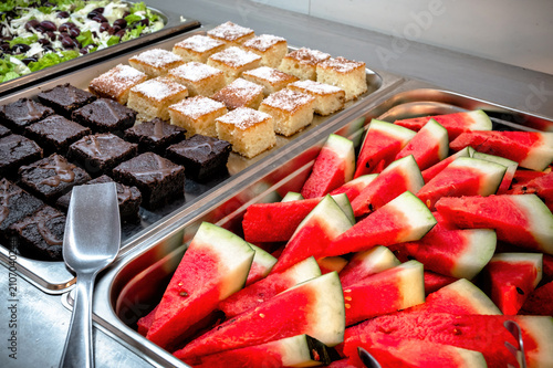 Modern buffet featuring watermelon slices, brownies and coconut sponge cake prepared for guests at a Mediterranean resort.