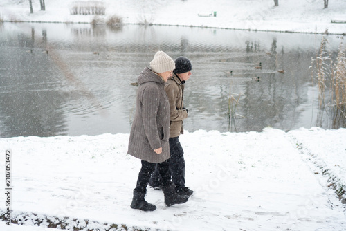 Senior couple walking arm in arm on snowy path. Love knows no age for a loving couple. Tenderness survives cold and affection warms more than clothing. Devoted partners embracing in winter landscape