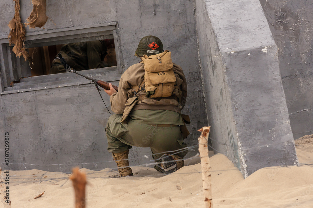Fototapeta premium Historical reenactment. A World War II-era American infantry soldier fights on a beach near a bunker