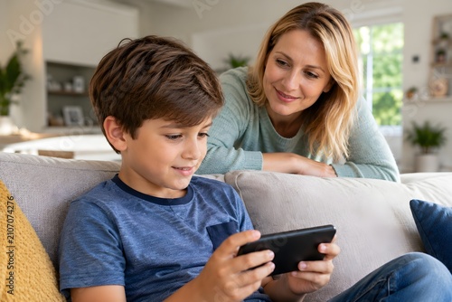 Mother Watching Son Using Smartphone on Sofa at Home
