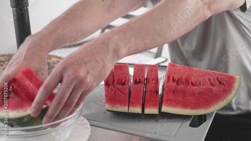 A person cuts a watermelon into even pieces using a knife and a cutting board in a home kitchen. The process shows careful handling and attention to each slice.
