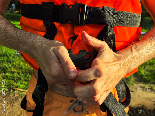 Quadro su tela Man fastening orange life jacket buckle with both hands outdoors, water safety a