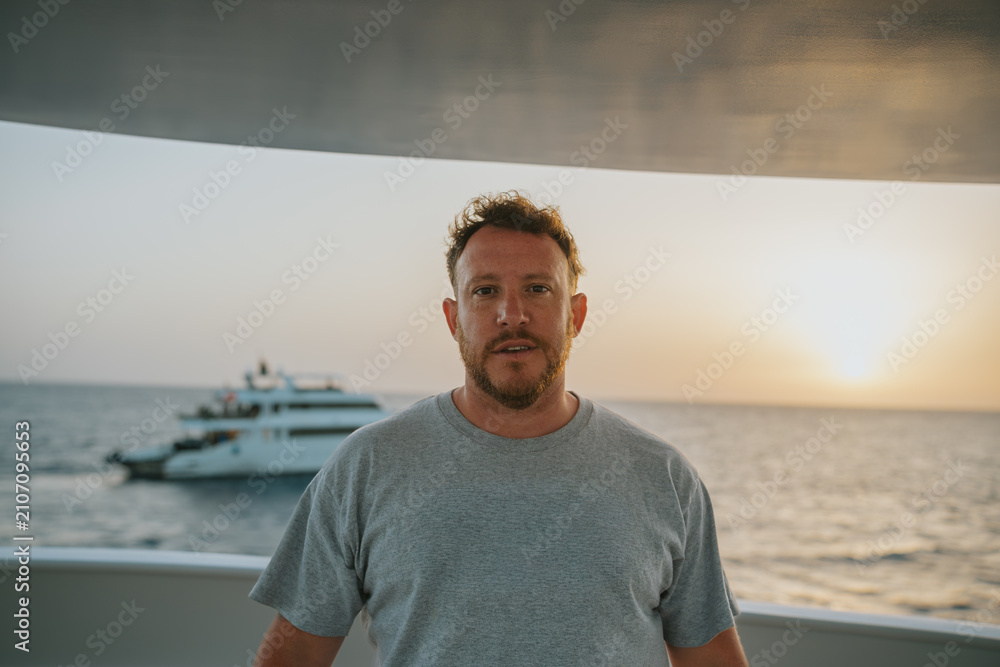 Fototapeta premium Man standing on a yacht deck, watching a golden sunset over the ocean