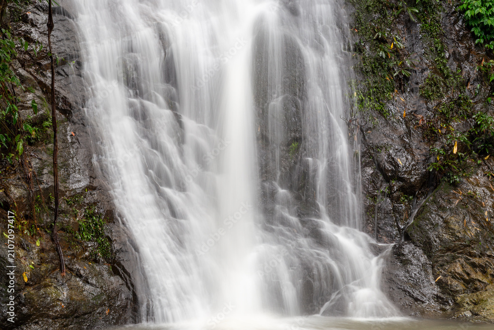 Obraz premium White water cascading over dark mossy rocks in a lush tropical forest waterfall.