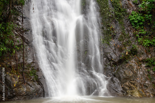 Long exposure photograph of a majestic waterfall flowing smoothly down rocky cliff in lush tropical rainforest.