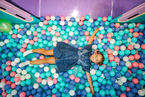 Canvas Print Little girl enjoying a colorful ball pit playtime while lying down