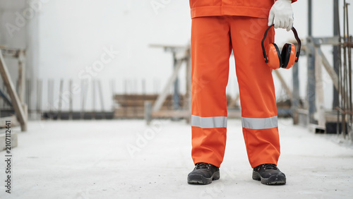 Worker in orange safety uniform holding earmuffs on construction site