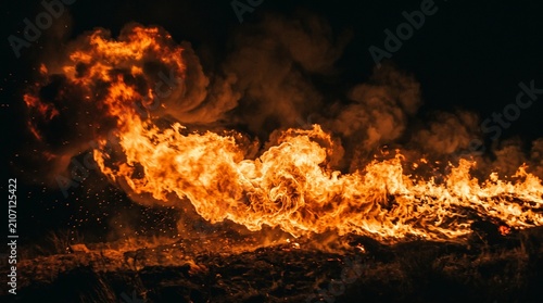 A horizontal stream of intense orange flames rolling across a black background with smoke.