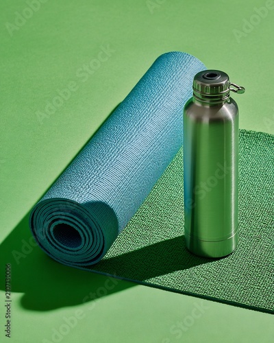 Rolled yoga mat and reusable water bottle on green background for fitness and wellness.