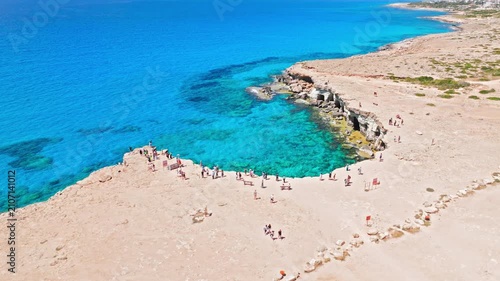 Aerial view of Cape Cavo Greco sea caves in Cyprus. Turquoise water, pale limestone cliffs and rocky coastal terrain create a bright Mediterranean landscape.