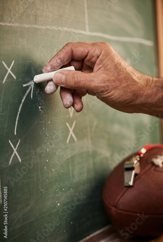 Coach drawing strategy on chalkboard with football in foreground  
