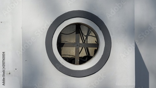 Tableau sur toile A circular window with a dark crossbar set into a white plaster wall with grey painted trim and soft shadows