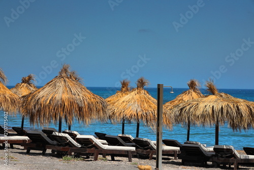 Straw umbrellas and lounge chairs on the beach in Santorini, Greece