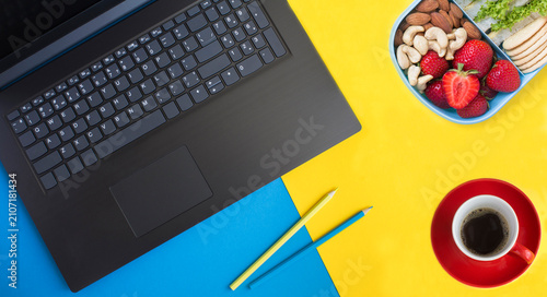 Office desk with laptop, pencils, coffee cup and lunch box on a colored background. Workspace desk. Top view.