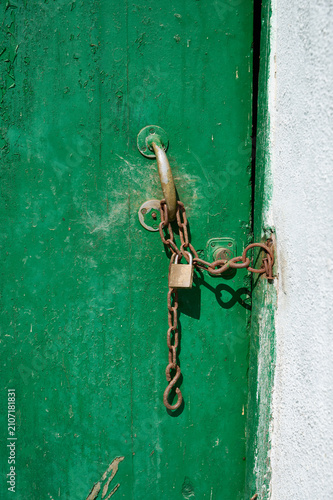Green wooden door secured by rusty chain and padlock