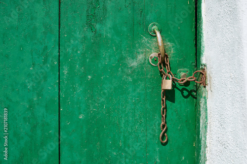 Old green door secured with rusty chain and padlock