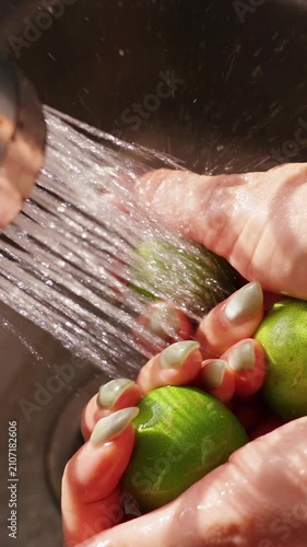 Vertical video. Close View of Female Hands Rinsing Fresh Green Limes under Spraying Water in Slow Motion, Clean Produce and Food Safety