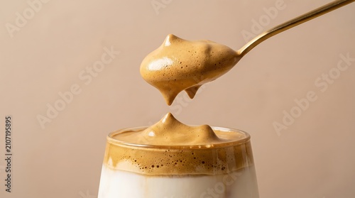 Creamy whipped coffee topping being drizzled from gold spoon into glass of cold milk beverage with displays close up view thick above glass with foam being lifted
