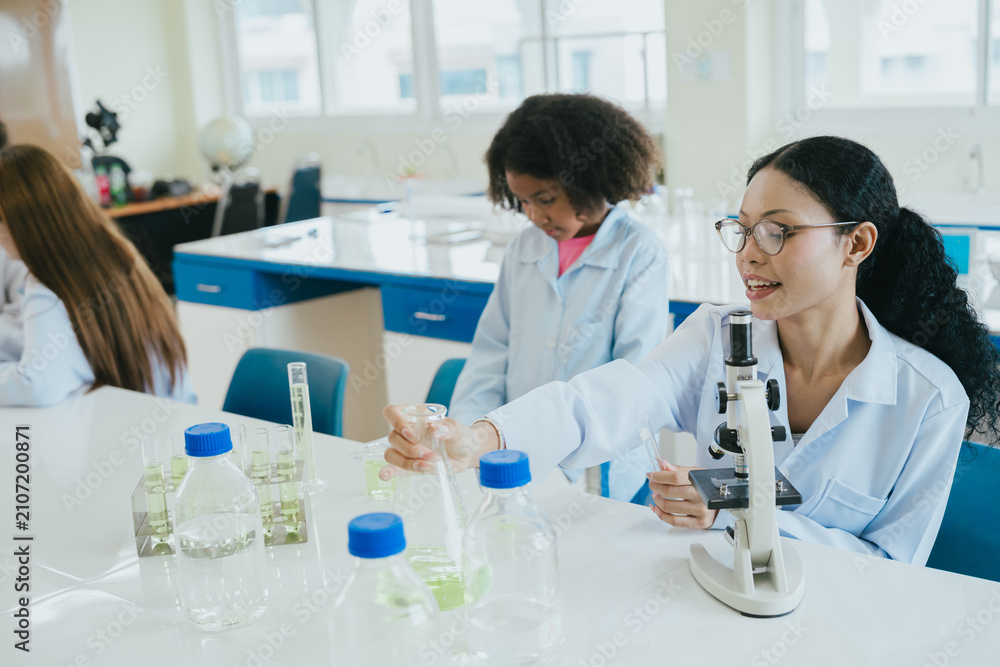 Fototapeta premium Laboratory scientist women in white coat using microscope during chemistry experiment in bright classroom