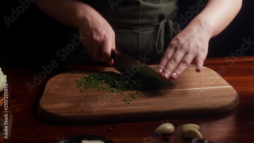 Close up of chef finely chopping fresh parsley on a wooden cutting board. Fresh herbs are prepared for homemade cooking in a cozy kitchen with natural ingredients.