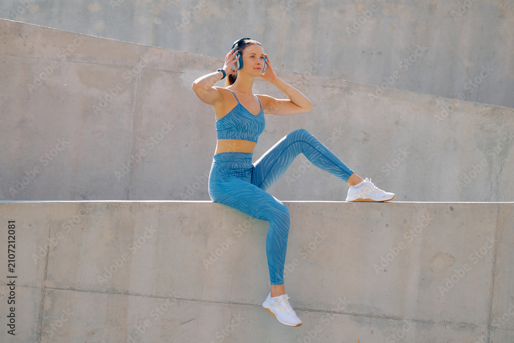 Fototapeta premium Sporty woman enjoying music while stretching outdoors at modern concrete structure