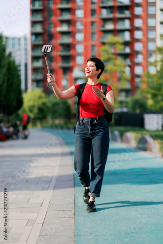 Woman vlogging with smartphone on selfie stick in city