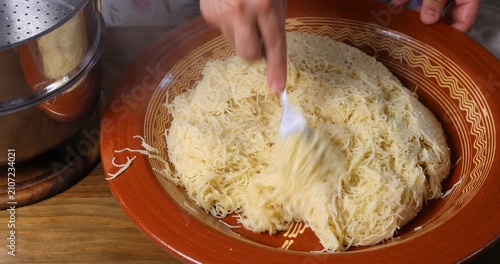Fluffing steaming hot Moroccan Seffa vermicelli with a fork in a traditional clay bowl