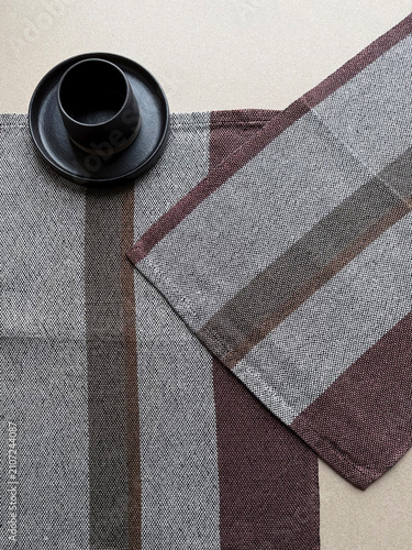 Black ceramic cup on striped linen napkins with natural textile texture. Minimal table setting featuring handmade stoneware and neutral tones for home decor, dining, hospitality and lifestyle projects