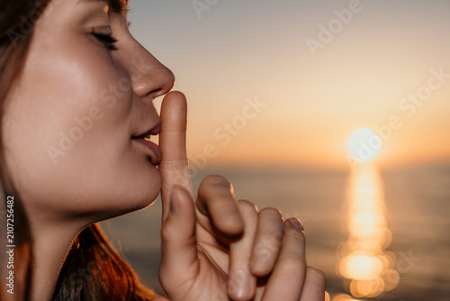 Obraz na plátne Silence woman sunset showing shh gesture with finger on lips at the beach during